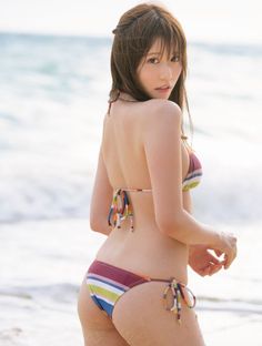 Woman in a striped bikini on a sandy beach, looking over her shoulder