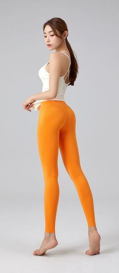 Woman in orange leggings and a white tank top posing in a studio