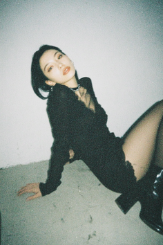 Woman in a black dress and fishnet stockings posing indoors