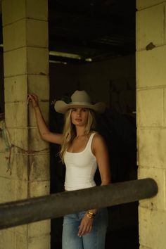 Woman in a cowboy hat and white tank top leaning against a pillar indoors