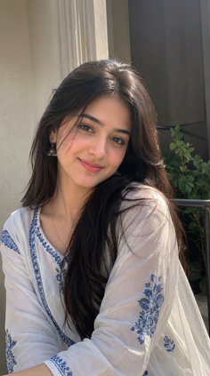 Young woman with long dark hair wearing a white top with blue embroidery outdoors