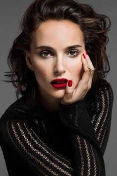 Woman with red lipstick and nails in a black top against a dark background