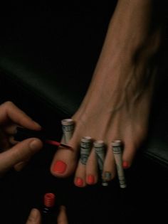 Person painting toenails with red polish, using rolled money as toe separators