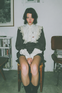 Woman with short dark hair wearing a lace-collared shirt and short skirt indoors