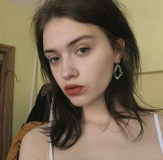Woman with dark hair and red lipstick wearing a white top and earrings