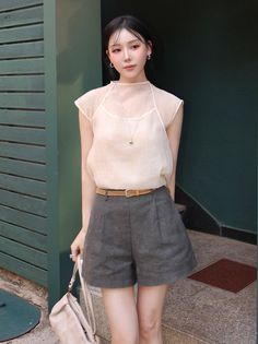 Woman in a sheer top and shorts with a braided belt standing outdoors