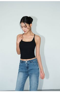 Woman in a black tank top and blue jeans posing in a studio