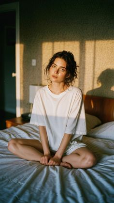 Woman with messy hair in a white t-shirt sitting on a bed with golden hour lighting