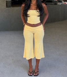 Woman in a yellow two-piece outfit with exposed midriff in an outdoor setting