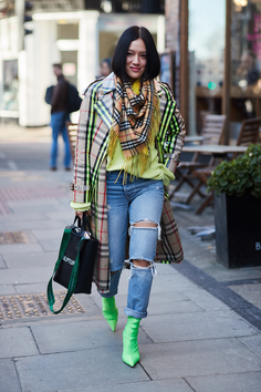 Woman in a plaid trench coat, ripped jeans, and neon green boots on a street