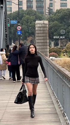 Woman in a black turtleneck and plaid skirt walking on a bridge