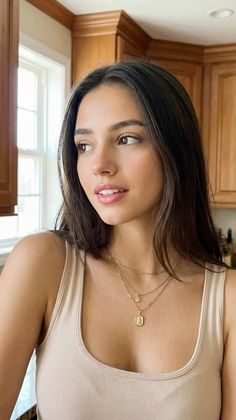 Woman with long dark hair and gold necklaces in an indoor setting