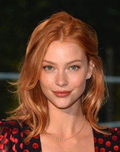 Woman with red wavy hair and green eyes wearing a polka dot top and necklace