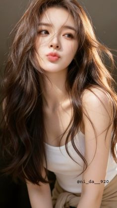 Woman with long brown hair and a white tank top, pursing her lips