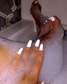 A person's feet and hand with white nails in a bubble bath