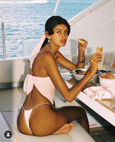Woman in a bikini top and thong bottom eating on a boat