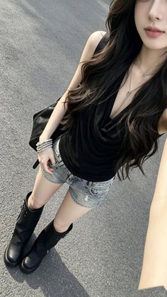 Woman with long dark hair wearing denim shorts and a black top outdoors