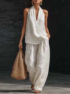 Woman in a white linen halter top and wide leg pants holding a straw bag