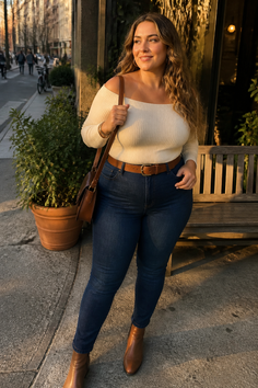 Woman in an off-shoulder top and jeans standing on a street at golden hour