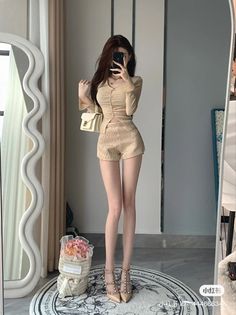 Woman in a beige top and gold shorts taking a mirror selfie indoors