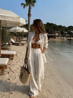 Woman in a white bikini and linen outfit walking on a sandy beach