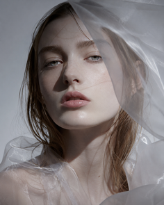 Woman with wet hair and sheer fabric draped around her, looking directly at the viewer