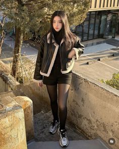 Woman in a black jacket and shorts with tights standing on outdoor stairs