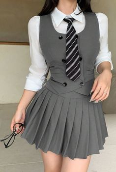 Woman in a gray school uniform with a striped tie holding glasses