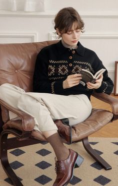 Woman in a black patterned cardigan reading a book in a brown leather chair