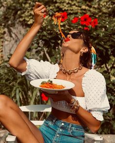 Woman eating pasta outdoors, wearing sunglasses and a white crop top