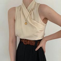Upper body shot of a person wearing a cream sleeveless top and black pants with a braided belt