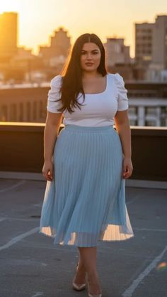 Woman in a white top and blue pleated skirt on a rooftop at golden hour