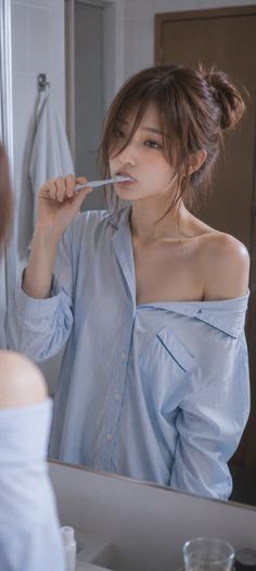 Woman in a light blue shirt brushing her teeth in a bathroom