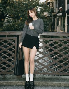 Woman in a gray cardigan and black mini skirt holding a cup outdoors