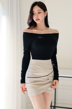 Woman with long dark hair wearing an off-shoulder top and mini skirt indoors