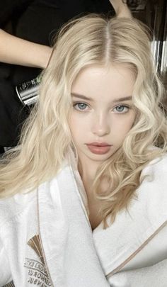 Blonde woman with blue eyes wearing a white bathrobe, looking at the camera