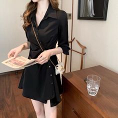 Woman in a black dress holding a newspaper indoors