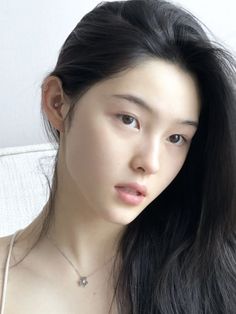 Woman with long black hair and a necklace, looking directly at the viewer