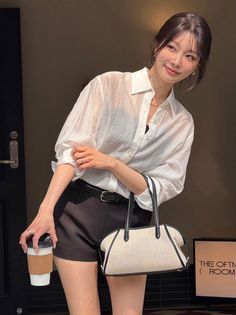 Woman in a white shirt and black shorts holding a coffee cup and bag