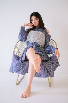Woman in a striped dress with exposed shoulders and legs sitting on a chair