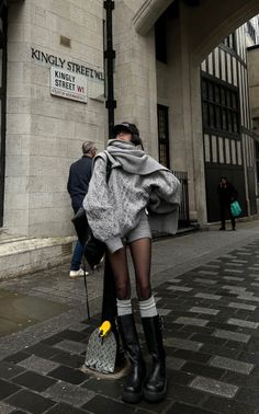 Woman in a grey cable knit sweater and black platform boots on a city street