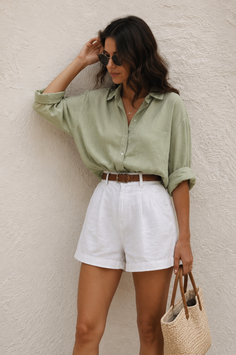 Woman in a green shirt and white shorts holding a straw bag outdoors