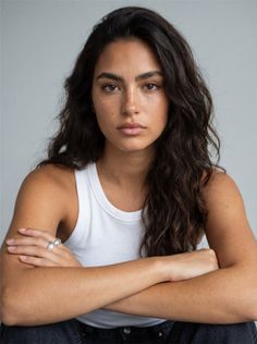 Woman with long wavy hair and freckles wearing a white tank top and silver ring