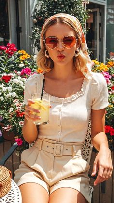 Woman with heart sunglasses and a head scarf holding a drink outdoors