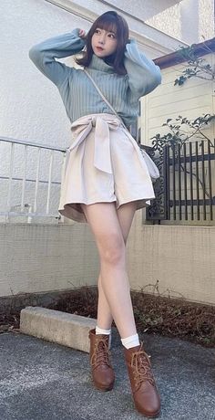 Woman in a light blue turtleneck and paperbag shorts posing outdoors