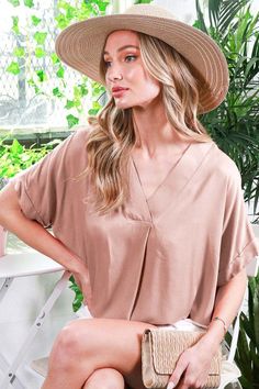 Woman in a straw hat and v-neck top holding a wicker clutch indoors