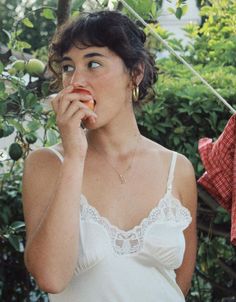 Woman in a white slip dress with lace trim eating an apple outdoors