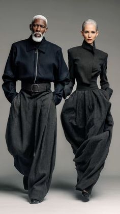 Two models in dark, wide-legged futuristic outfits in a studio