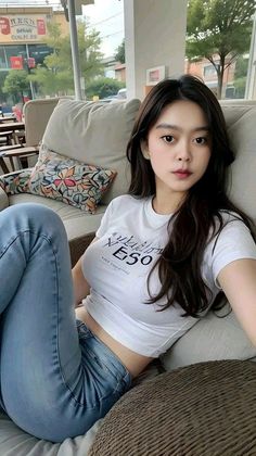 Woman with long dark hair wearing a white t-shirt and jeans, sitting indoors