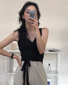 Woman in a black top and beige pants taking a mirror selfie indoors